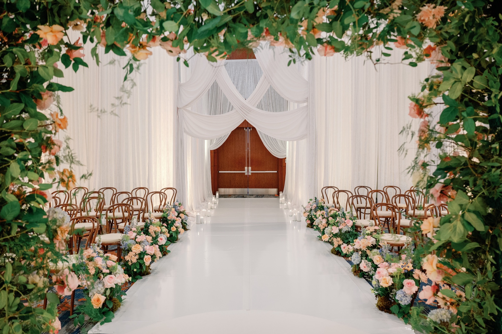 Hilton Baltimore ballroom transformed with draped white fabric, a garden floral arch, and a white aisle lined with florals
